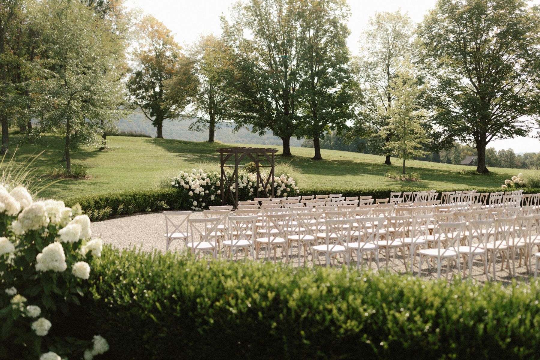 Event setup with white folding chairs arranged on green grass with trees and hills in background